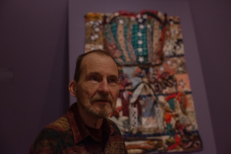 A photo of a man. A quilt is in the background.
