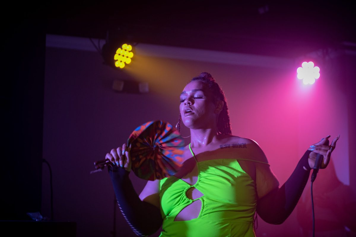 A person wearing a green top stands fanning themselves, they're in a nightclub and lights are shining on them.