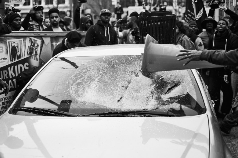A picture of someone smashing a police car with a traffic cone.