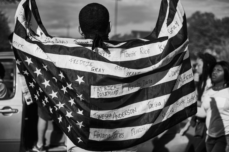 A man drapes an American flag on his shoulders. It has the names of Black people who died as a result of police violence.