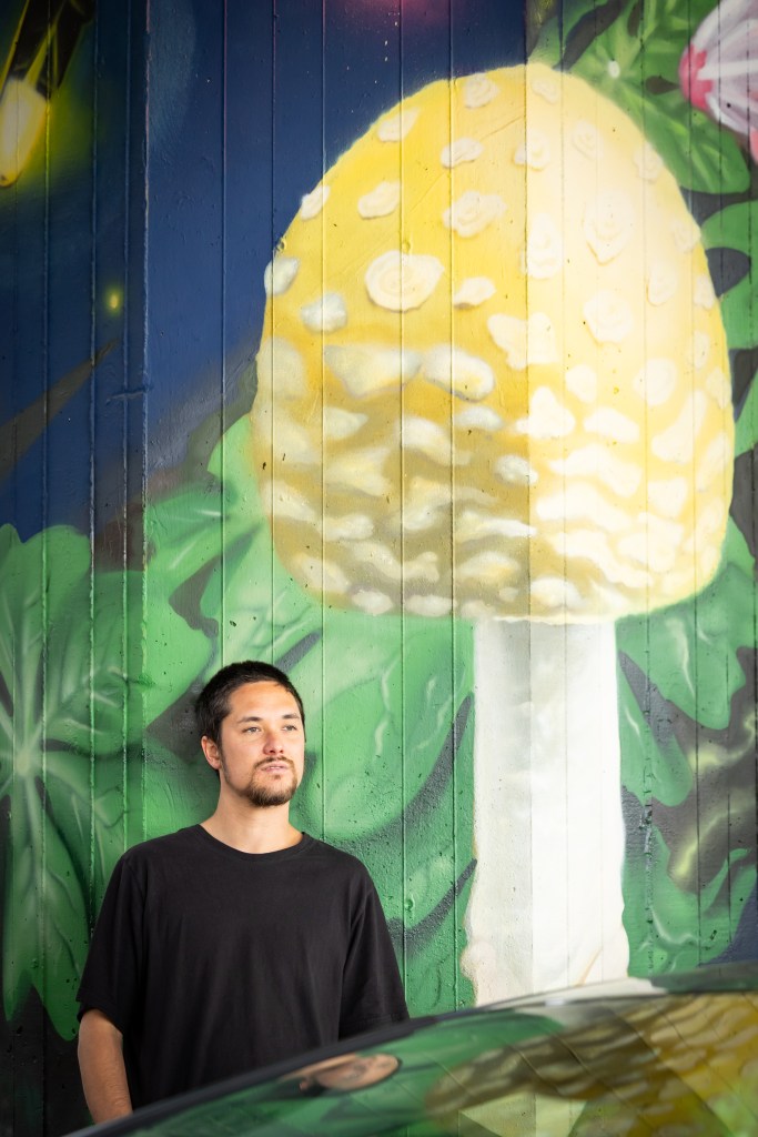 Hiro Hubbard stands next to painting he made of a large mushroom on a pillar under the Jones Falls Expressway.