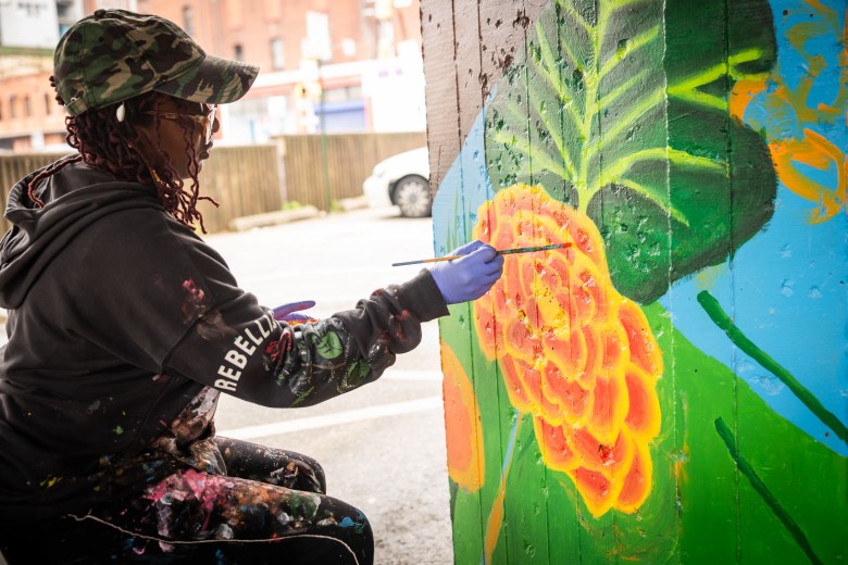 Hope McCorkle paints a flower on a pillar under the Jones Falls Expressway.