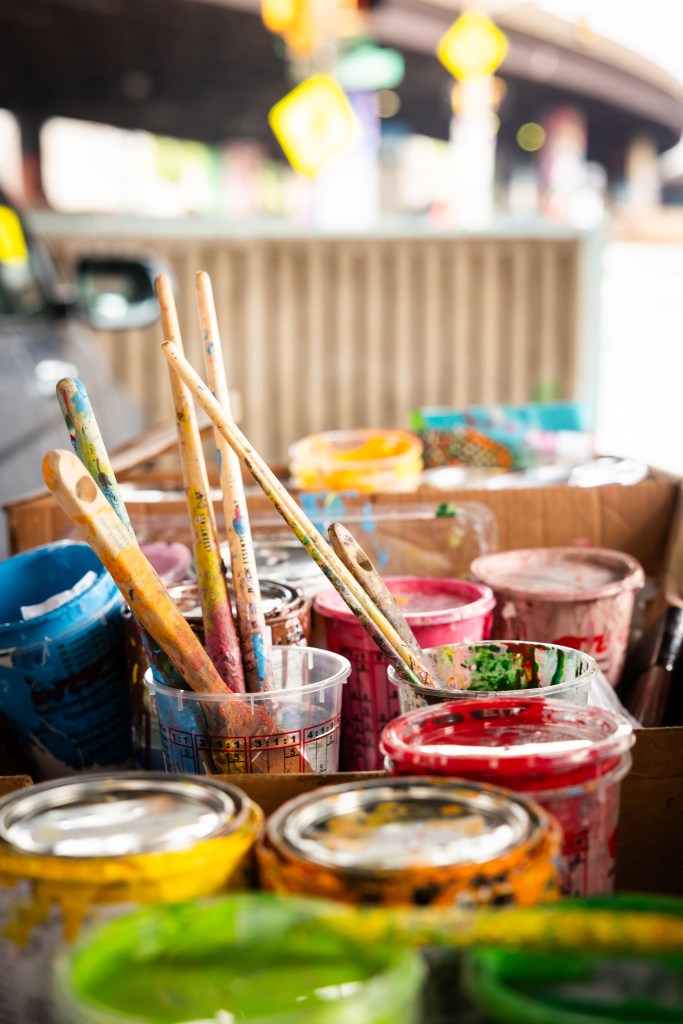 Various used paint brushes in cups and paint cans.