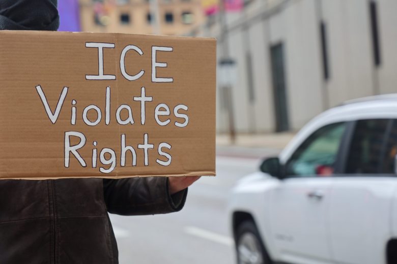 A person holding a cardboard sign that says "ICE violates rights"