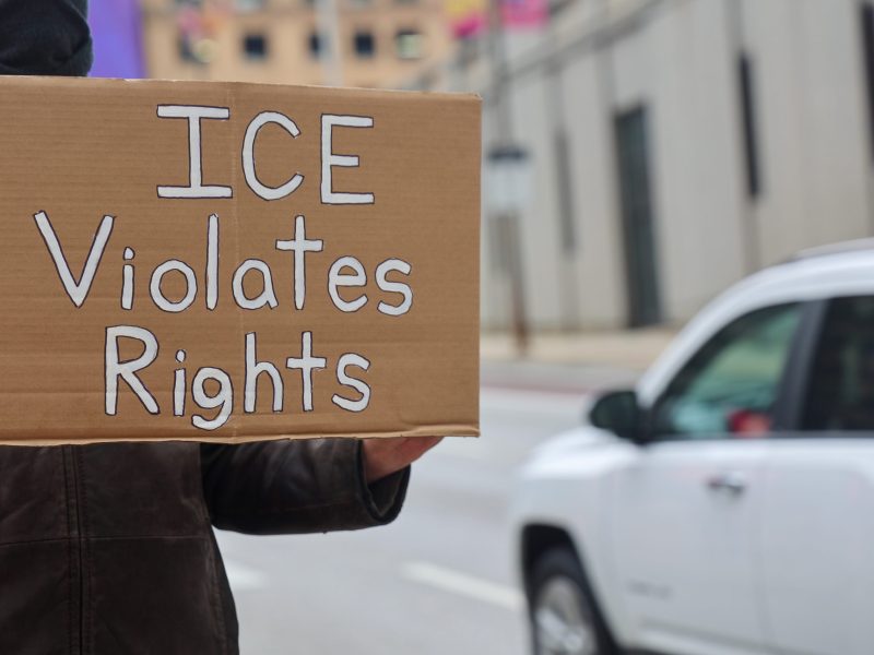 A person holding a cardboard sign that says "ICE violates rights"