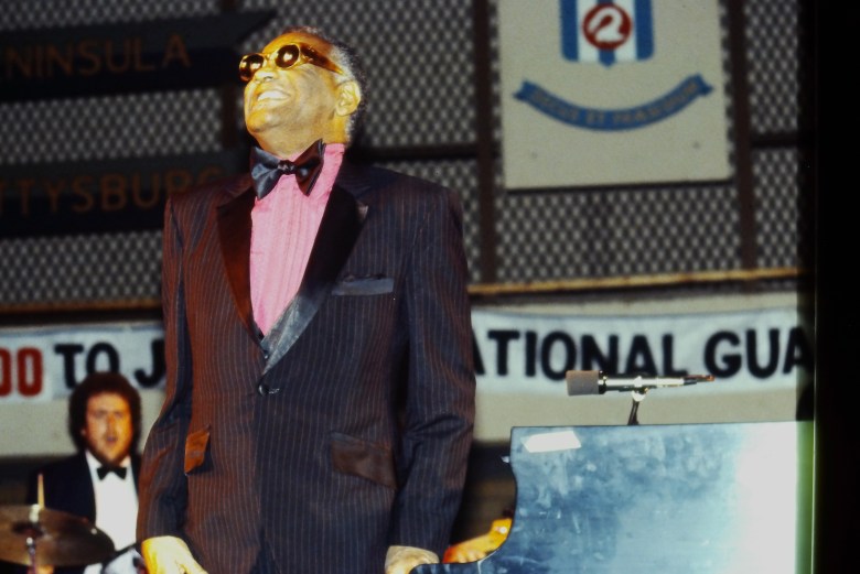 Ray Charles stands on stage wearing a suit.