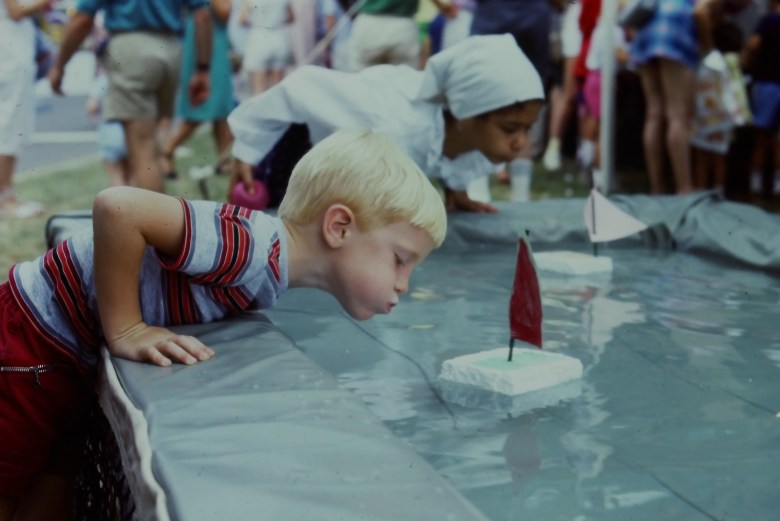 Children blow air out of their mouths to push styrofoam boats in water during the 1985 Artscape. Image courtesy of the Baltimore Office of Promotion & Arts.