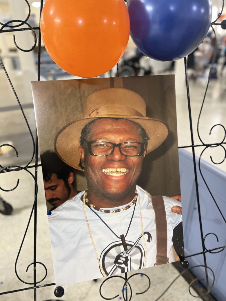 A framed photo of A photo of Anthony Wann Williams on display at his Aug. 22 celebration of life. Two balloons, one orange and one blue, are attached to the frame. Williams is a smiling Black man.