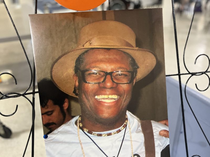 A framed photo of A photo of Anthony Wann Williams on display at his Aug. 22 celebration of life. Two balloons, one orange and one blue, are attached to the frame. Williams is a smiling Black man.