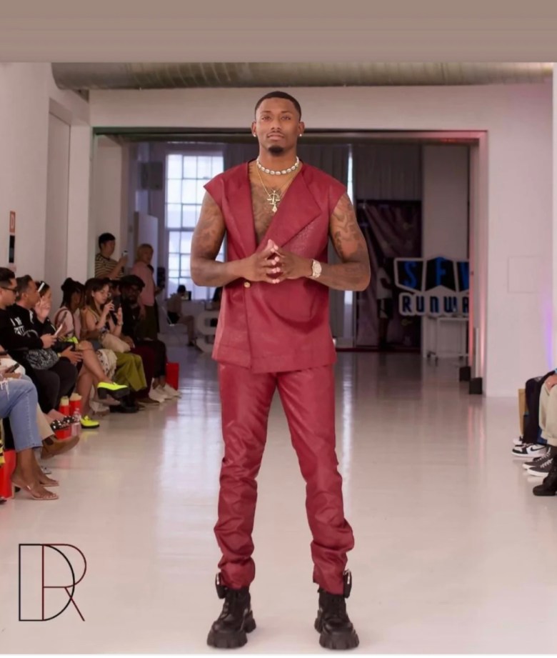 A photograph of a man on a runway wearing a red leather suit. 