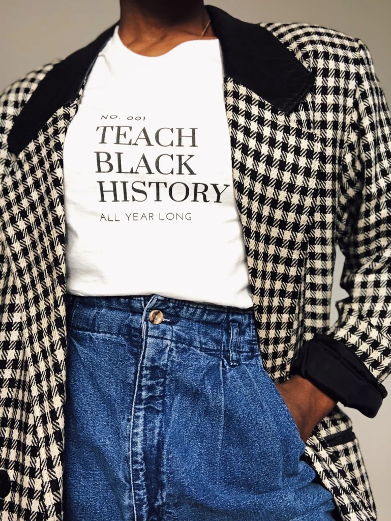Photograph of a woman with brown skin wearing a tshirt that says "teach black history all year long" 