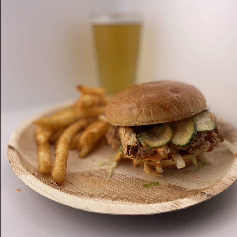 A sandwich and fries on a tan plate with a glass of beer in the background.