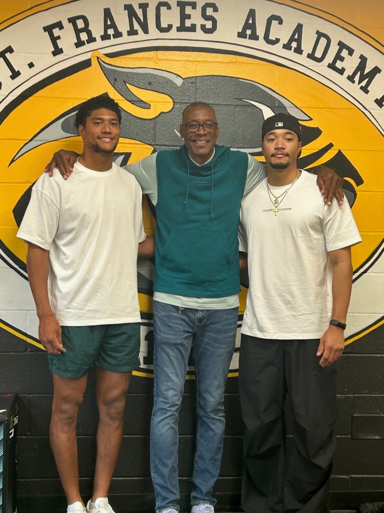 Three people pose in front of St. Frances Academy's team logo.