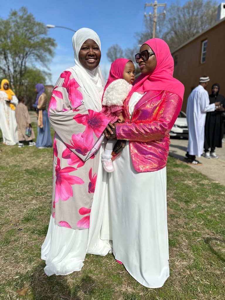 Two women and a baby girl, dressed all in pink and white.