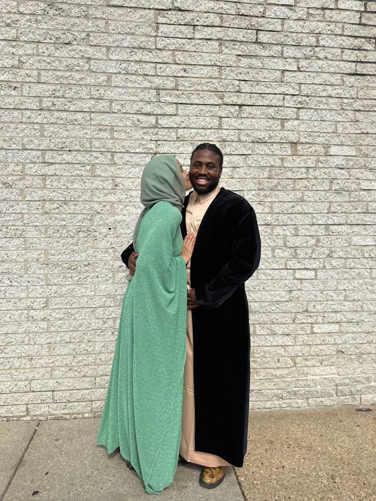 A couple poses in front of a brick