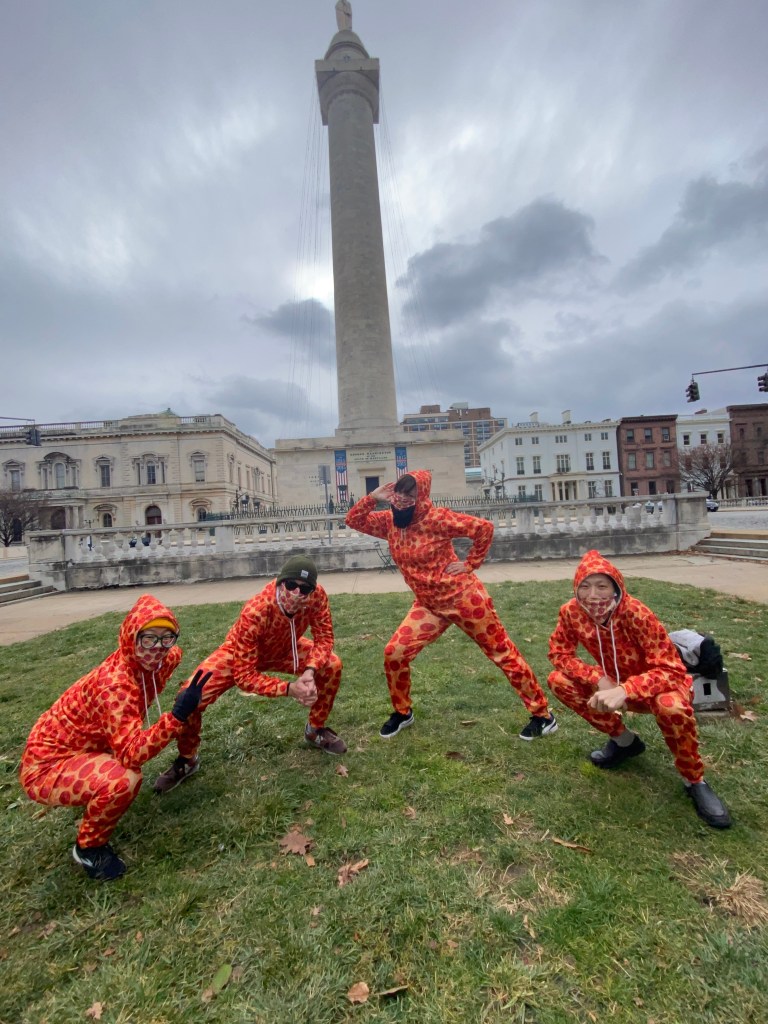 Four people pose in front of the Washington Monument wearing red onesies. 