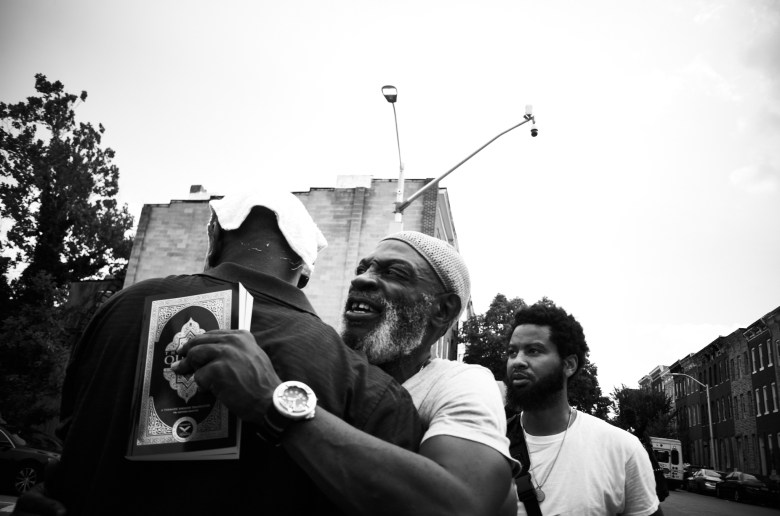 Two men embrace. One holds a copy of the Quran.