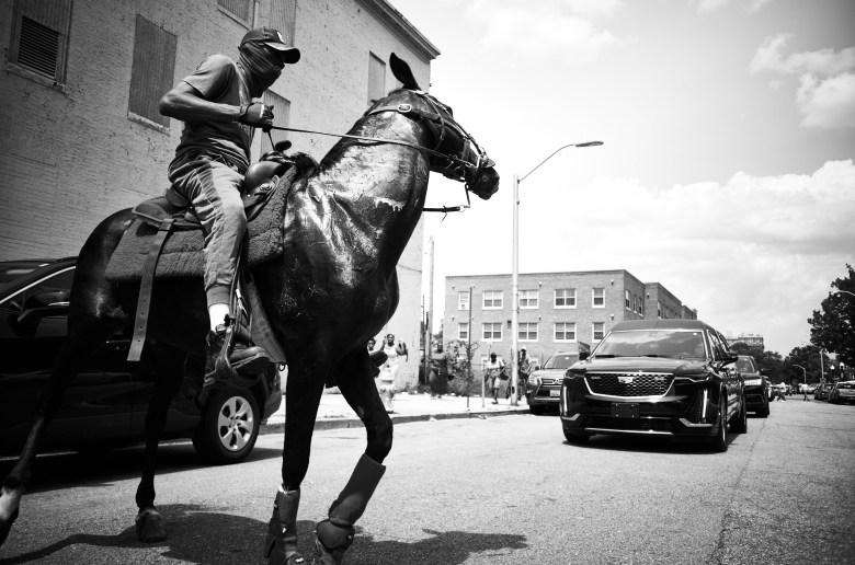 A man on horseback. A funeral hearse can be seen in the background.