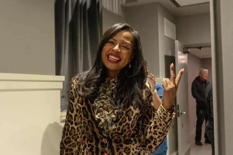 A woman with brown skin flashes a peace sign at the camera