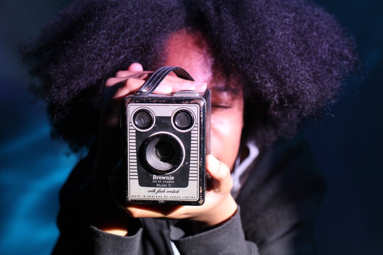 A person with brown skin and brown hair holds a camera
