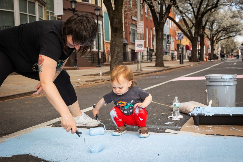 An adult and child paint on the street.