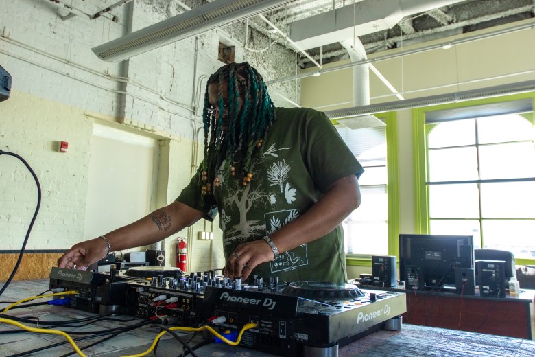 A person with brown skin at a plays a set of CDjs