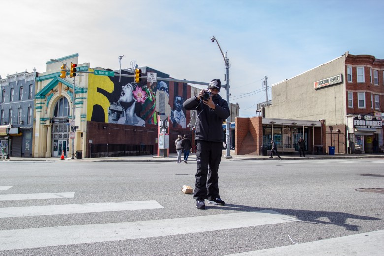 Shaun Young, a Black man, holds his camera up as if he is taking a photo.