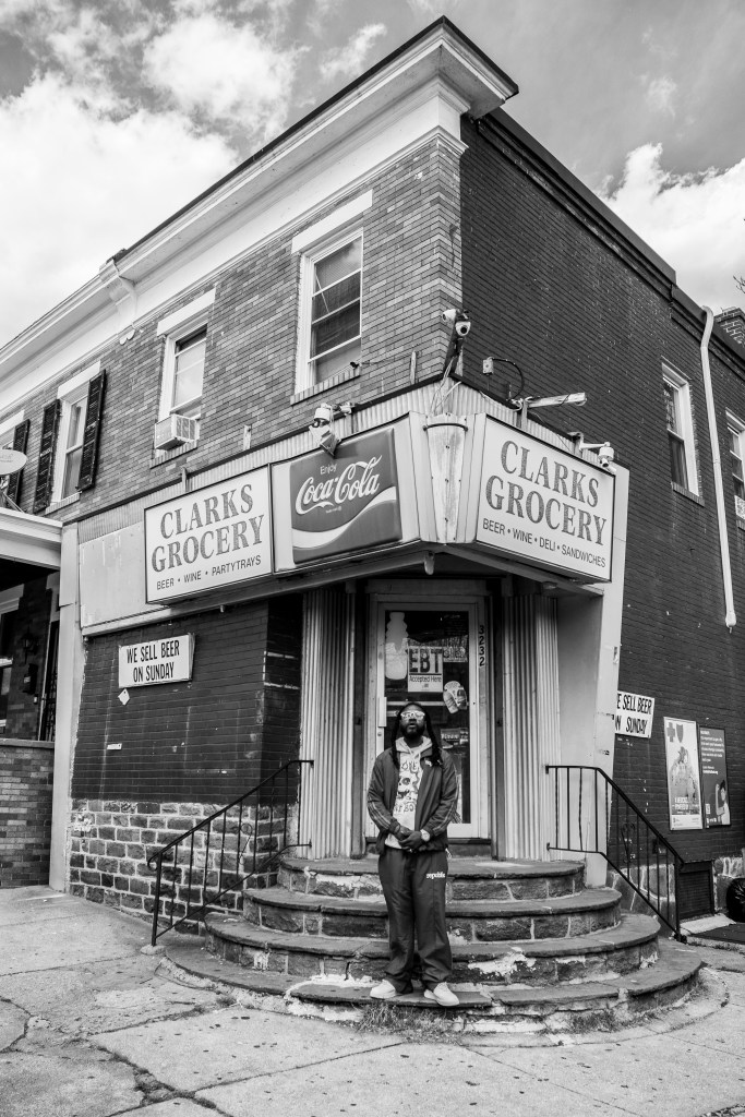 photo of a man with brown skin posing in front of a store. 
