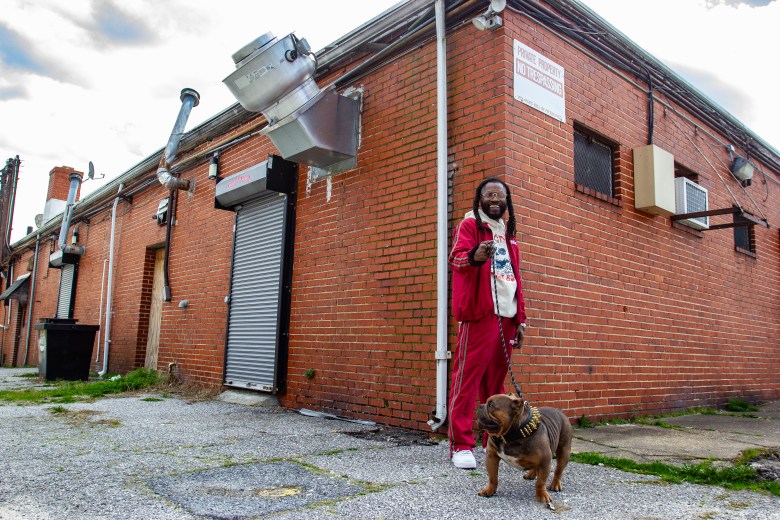 Photo of a man with brown skin smiling and holding a dog leash. 