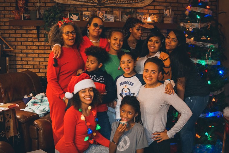 A family poses for a holiday photo. They are of various ages and have brown skin. They are in holiday dress. 
