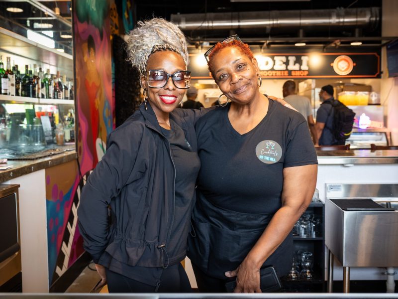 Two women dressed all in black pose for a photo.