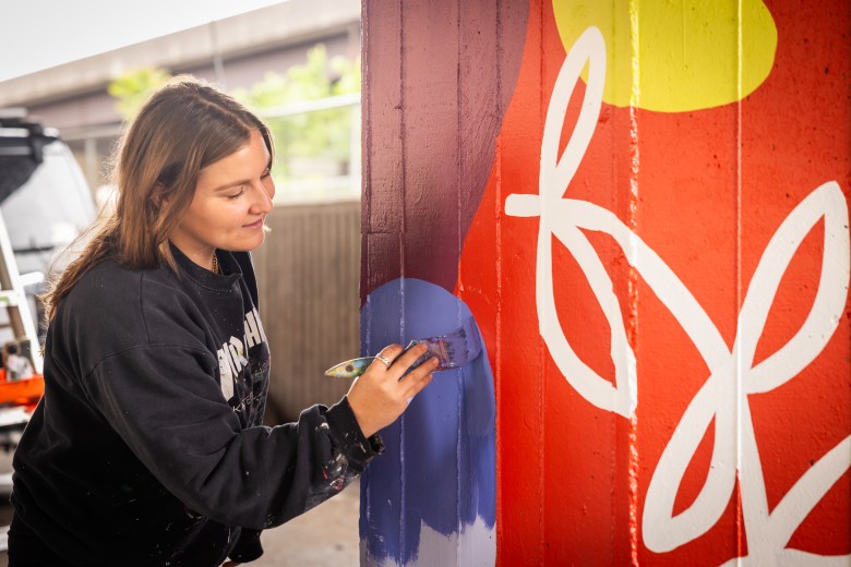 Paige Orpin painting her mural on a pillar under the Jones Falls Expressway.