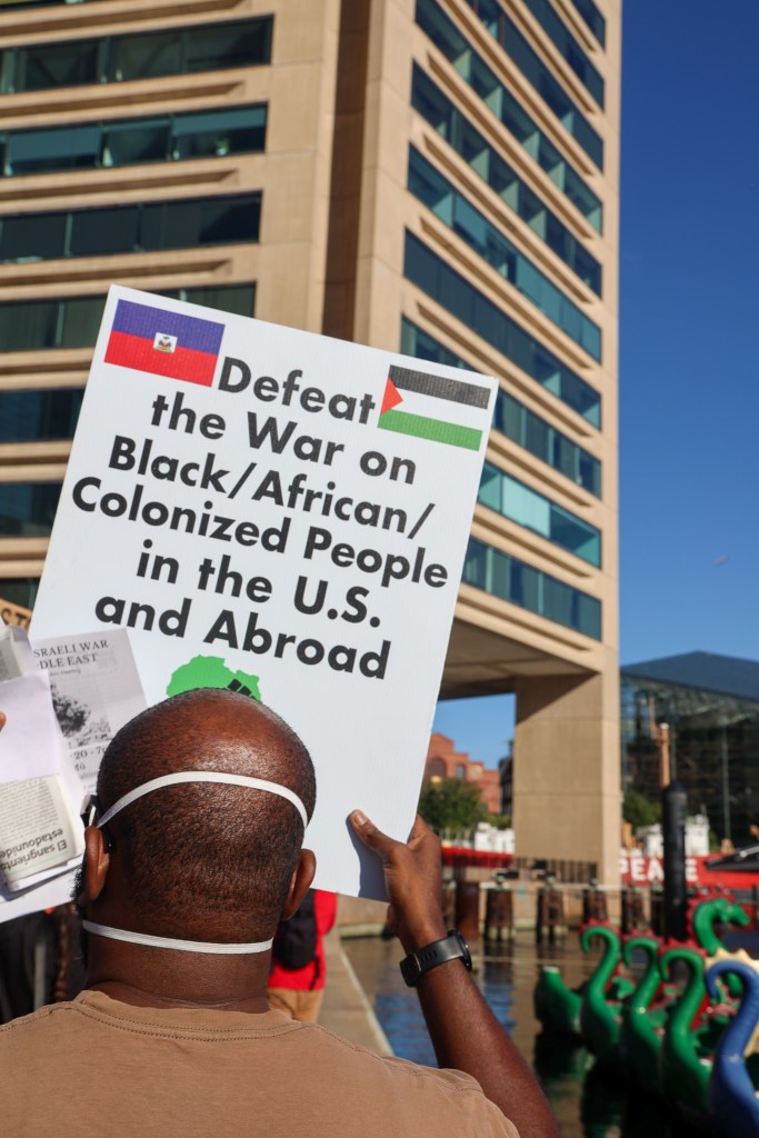 A person holds a sign that reads "Defeat the war on Black/African/Colonized People in the U.S. and abroad"