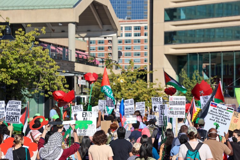 A group of people march holding signs at the Baltimore Inner Harbor.