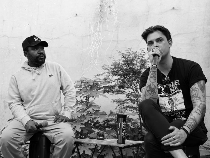One man speaks into a microphone and another man watches.