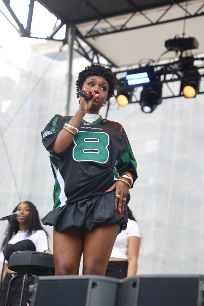 A person wearing black and green jersey and a black skirt holds a mic