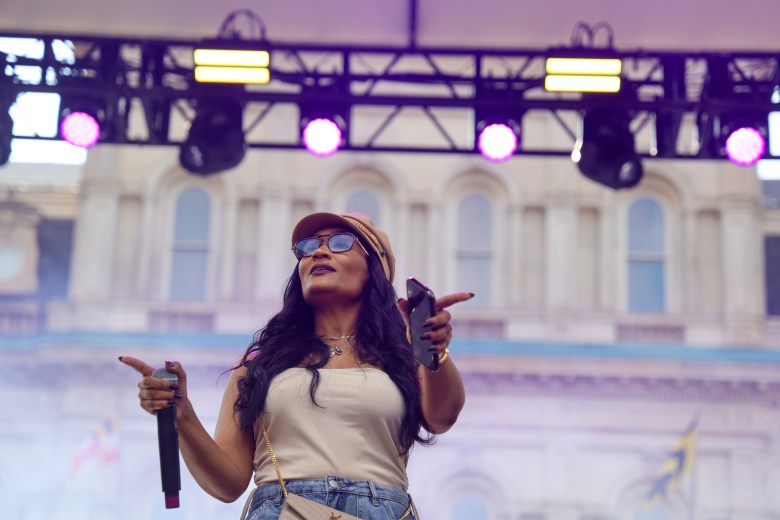 A woman stands on stage holding a mic. and cell phone.