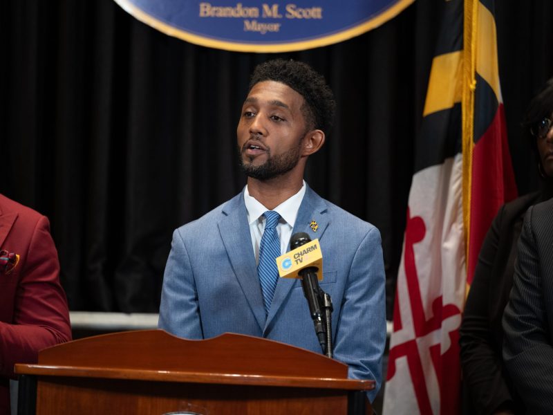 A photo of a Black man wearing a blue suit standing at a podium.