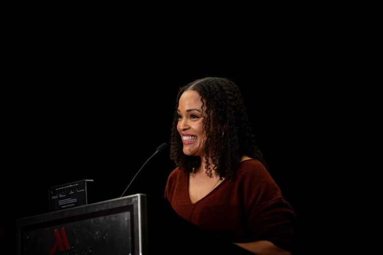 A photo of author Jesmyn Ward. She is a smiling Black woman with curly hair wearing a burgundy top.