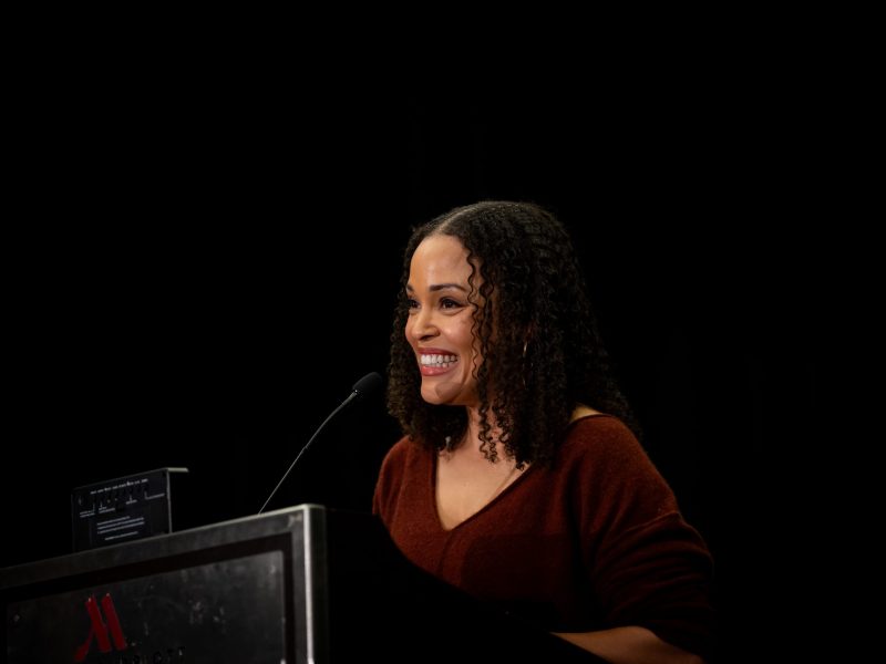 A photo of author Jesmyn Ward. She is a smiling Black woman with curly hair wearing a burgundy top.