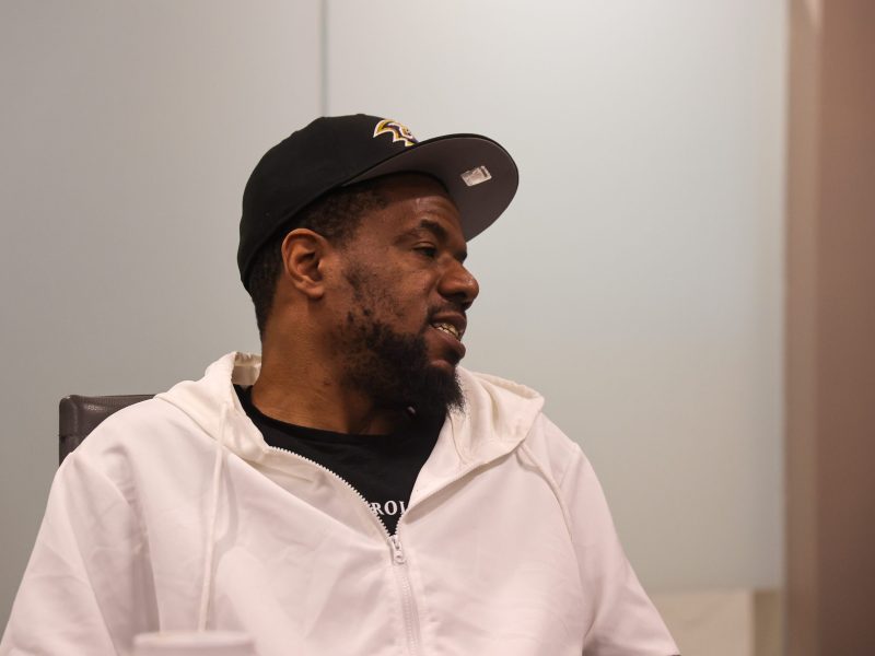 A Black man wearing a black baseball cap and a white shirt speaks.