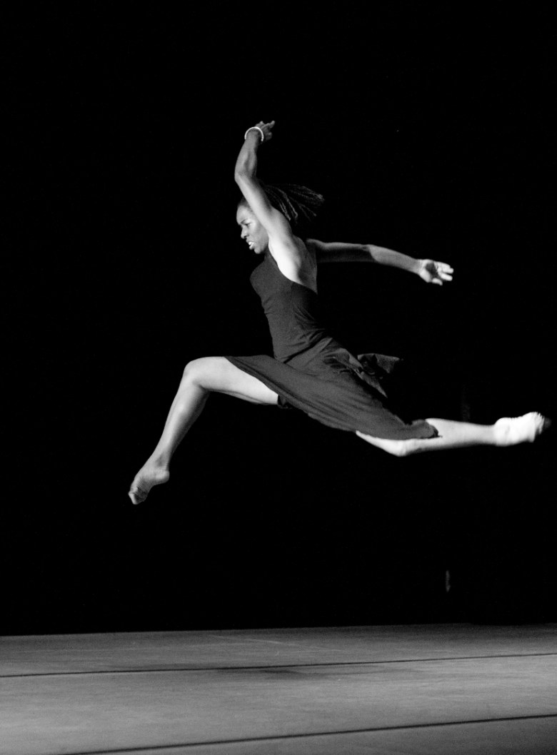 a ballerina with brown skin dances across a stage