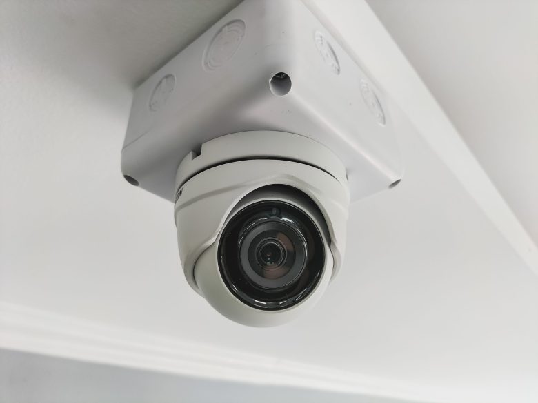 A white CCTV camera on the ceiling inside the building.