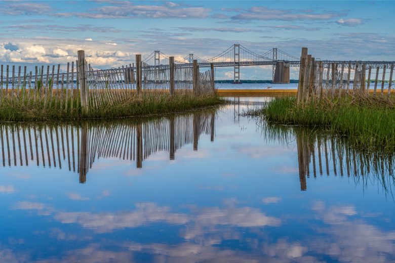 The sky reflects off a body of water with a large bridge in the background.