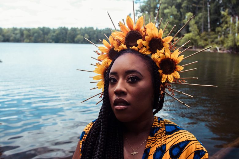 A woman with brown skin and a floral crown near a body of water