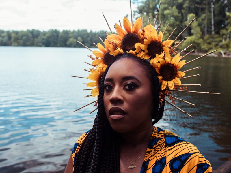 A woman with brown skin and a floral crown near a body of water