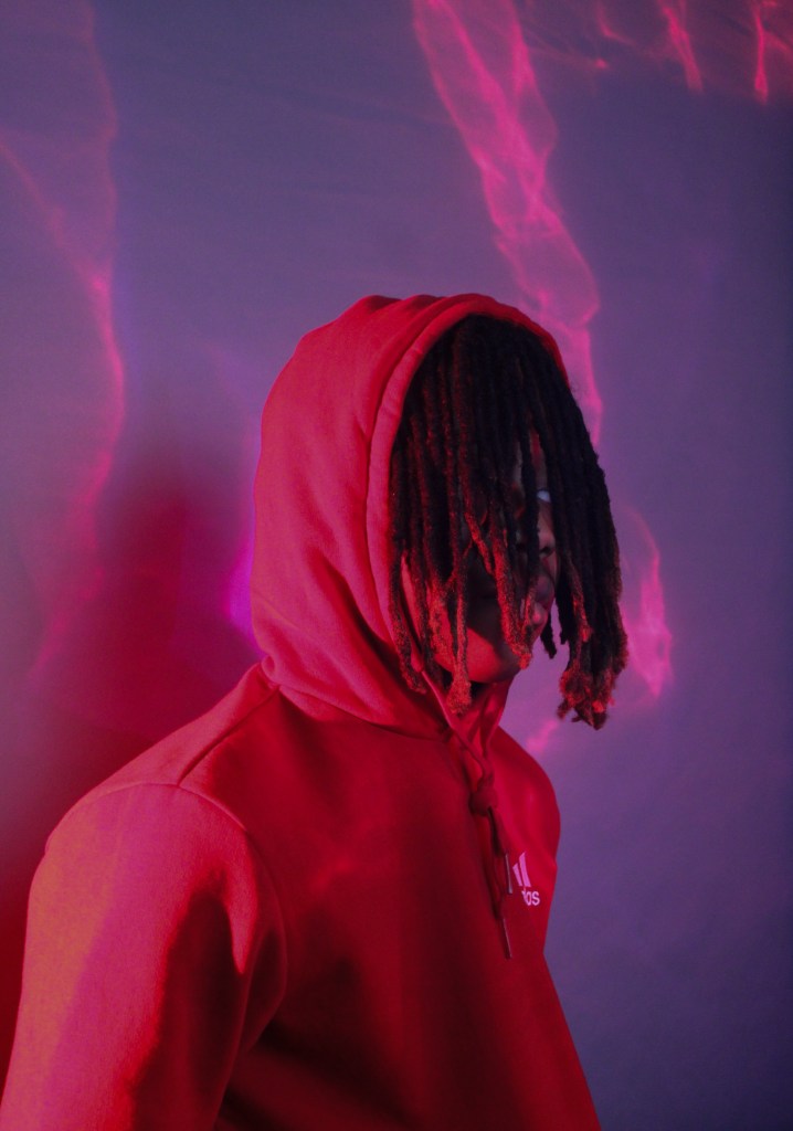 A person with brown skin and brown hair wears a hoodie.