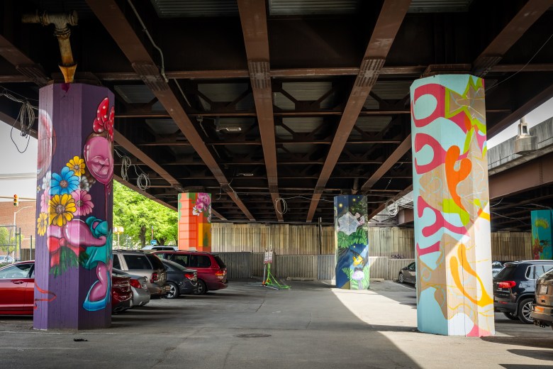 Several different colorful murals on the pillars under the Jones Falls Expressway.