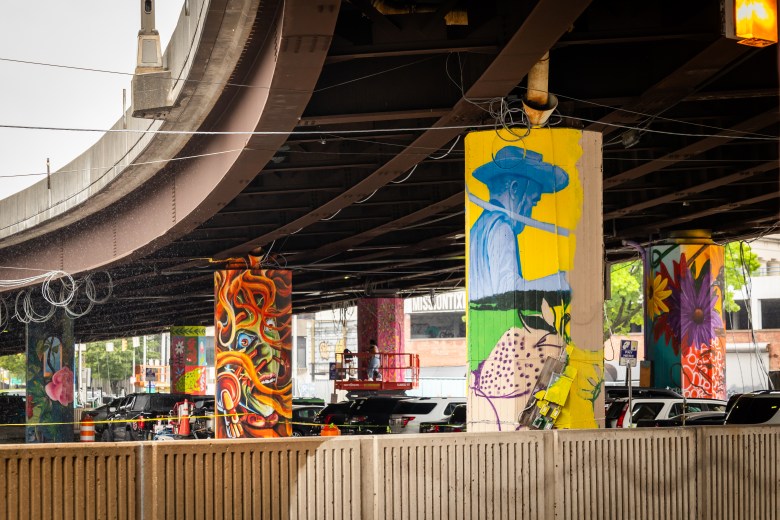 Several different colorful murals on the pillars under the Jones Falls Expressway.
