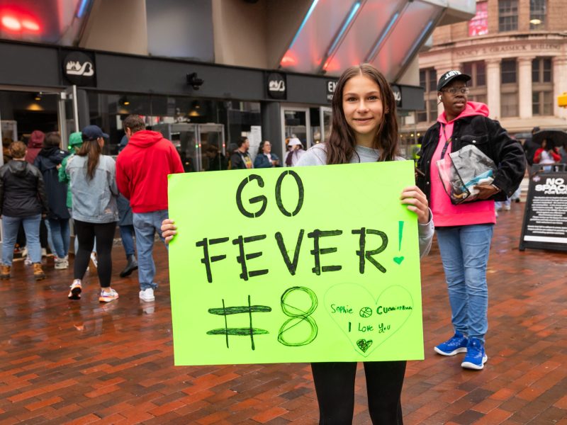 A smiling young person holds a sign that says "go fever #8"